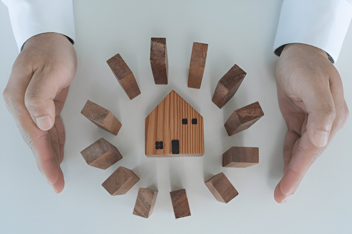 Protective hands around a wooden house model representing rental damage deposit security with Chelton Brown.